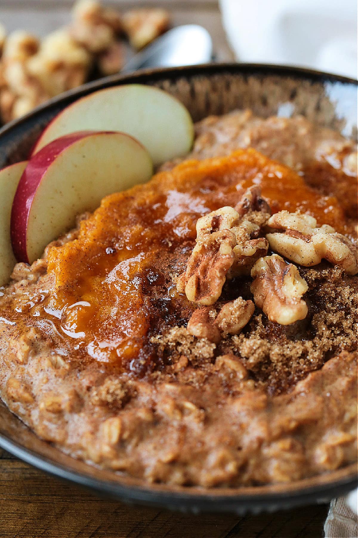 Pumpkin Oatmeal is so hearty and comforting, and only takes 10 minutes to make! A cozy, healthy breakfast with all your favorite fall flavors! A bowlful of pumpkin oatmeal topped with apples, walnuts and pumpkin puree, with a spoon.
