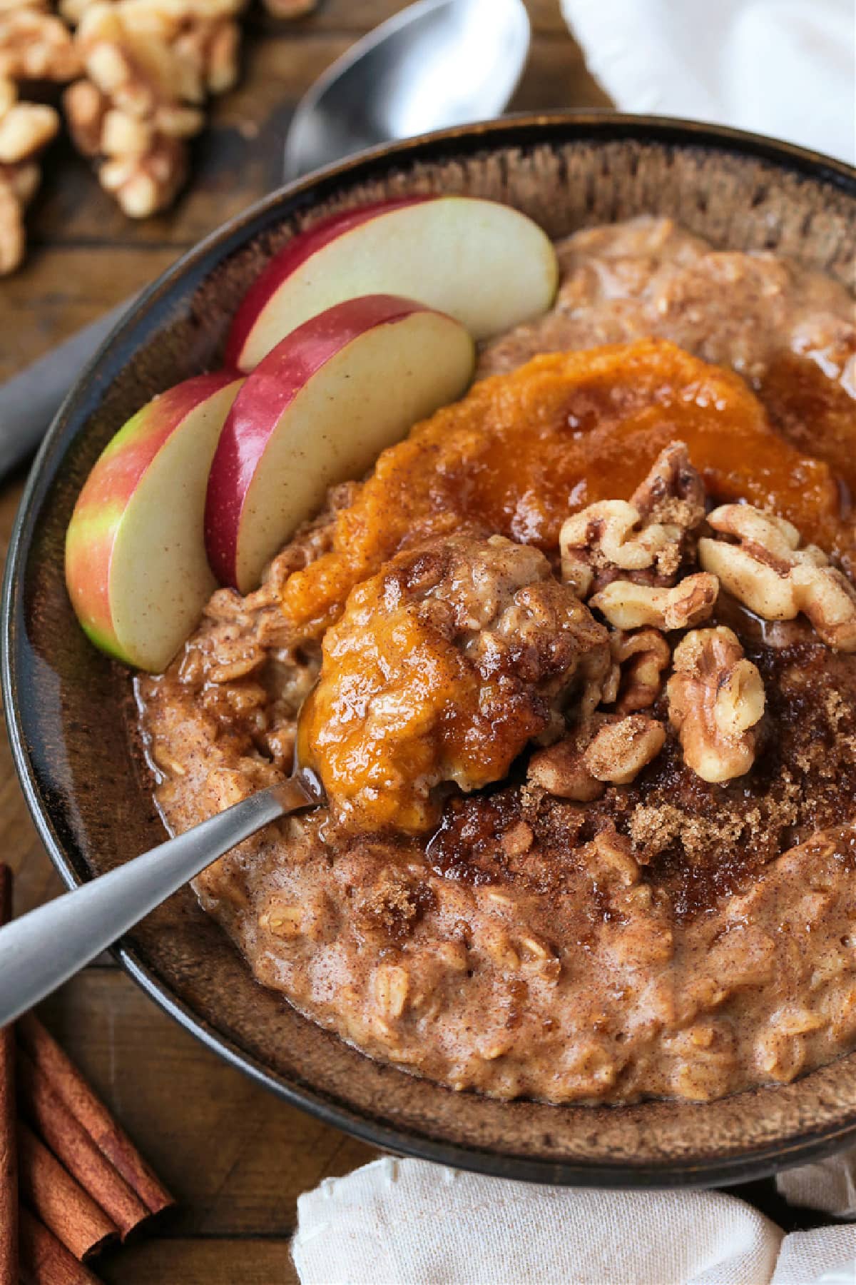 Pumpkin Oatmeal is so hearty and comforting, and only takes 10 minutes to make! A cozy, healthy breakfast with all your favorite fall flavors! A bowlful of pumpkin oatmeal topped with apples, walnuts and pumpkin puree, with a spoon.