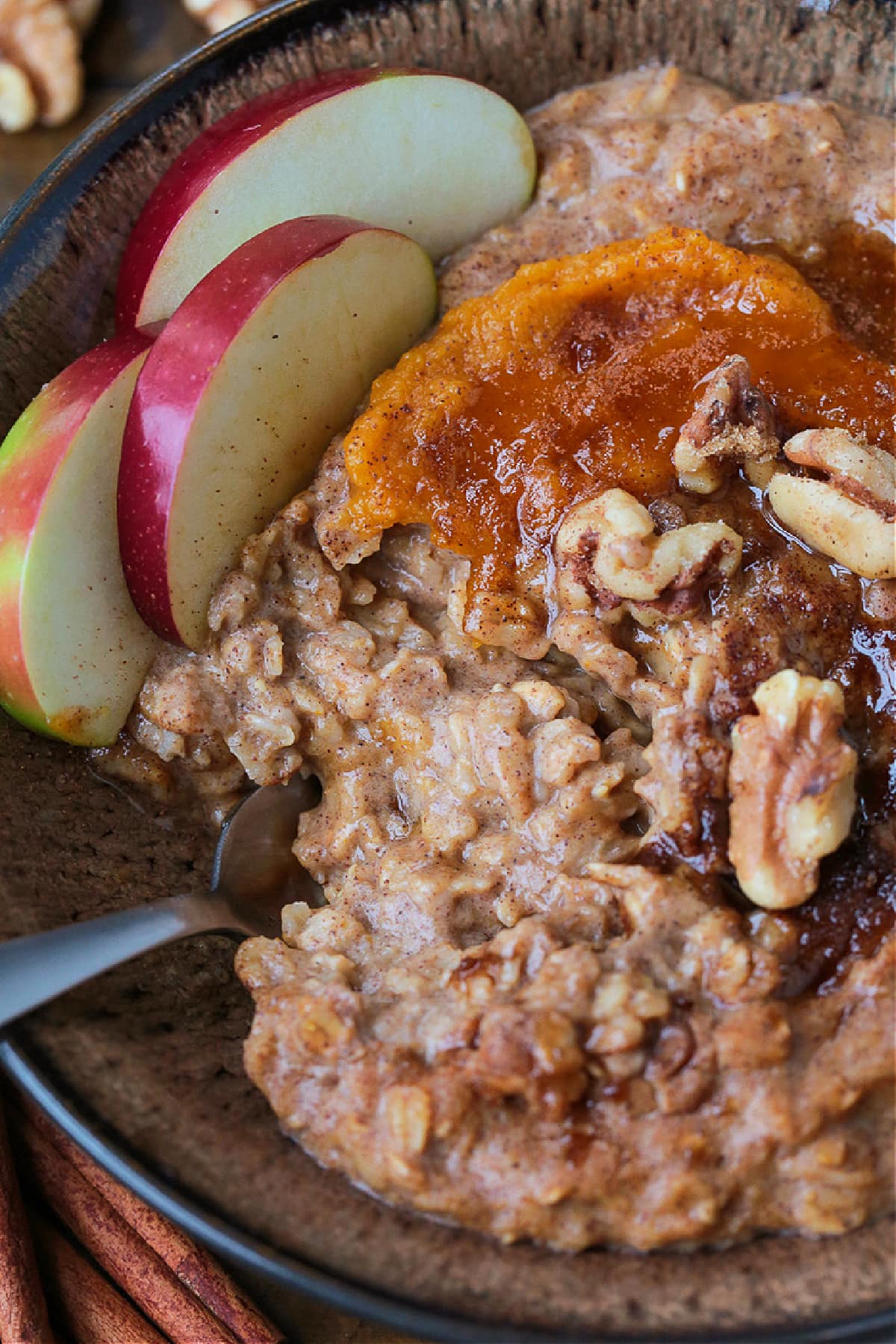 Pumpkin Oatmeal is so hearty and comforting, and only takes 10 minutes to make! A cozy, healthy breakfast with all your favorite fall flavors! A bowlful of pumpkin oatmeal topped with apples, walnuts and pumpkin puree, with a spoon.