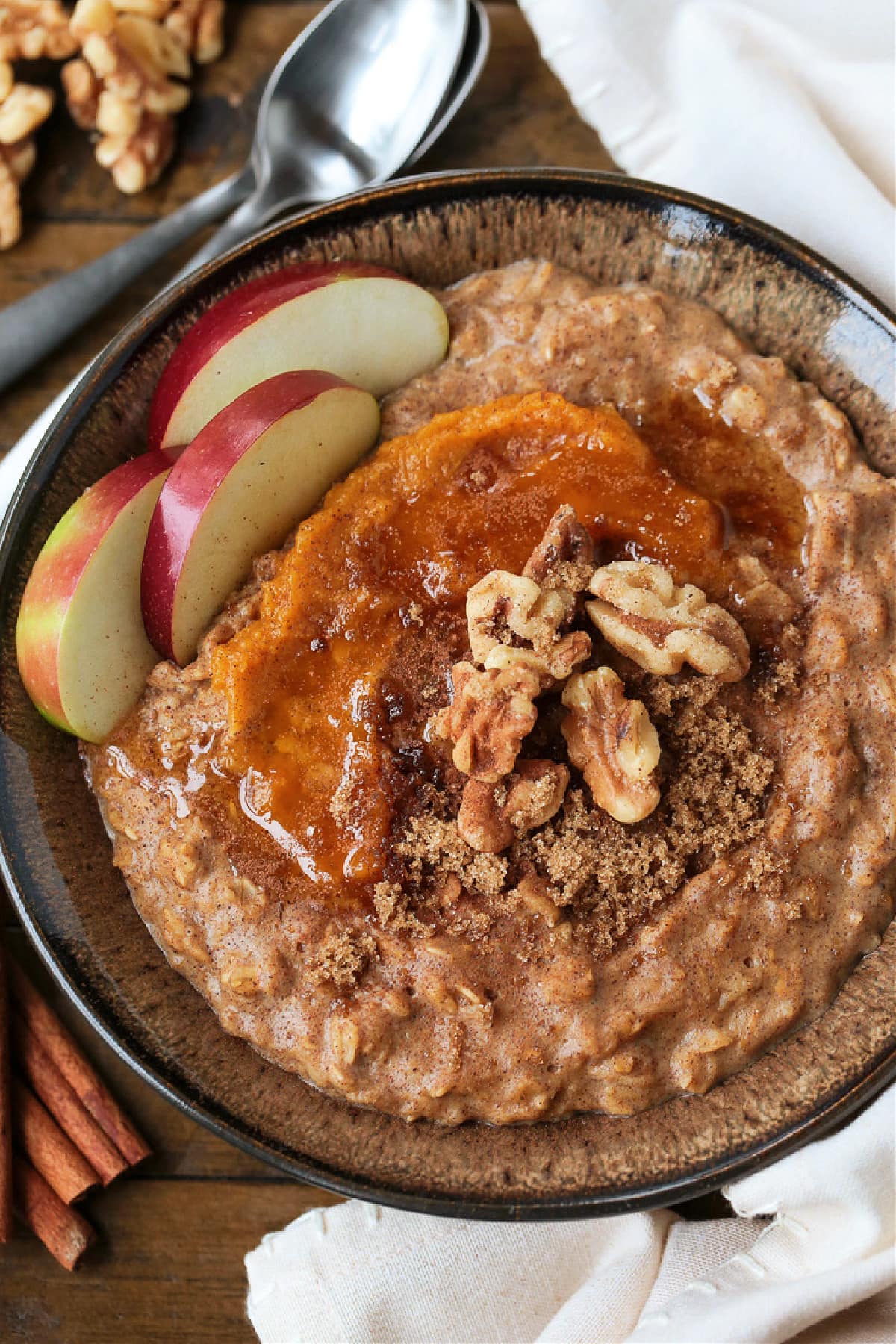 Pumpkin Oatmeal is so hearty and comforting, and only takes 10 minutes to make! A cozy, healthy breakfast with all your favorite fall flavors! A bowlful of pumpkin oatmeal topped with apples, walnuts and pumpkin puree, with a spoon.