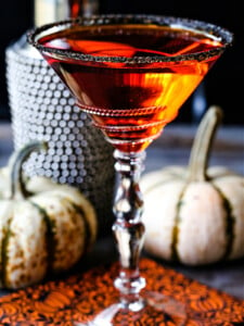 an orange martini in a sugar rimmed glass with pumpkins in the background