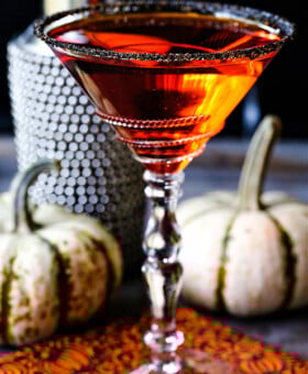 an orange martini in a sugar rimmed glass with pumpkins in the background