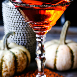 an orange martini in a sugar rimmed glass with pumpkins in the background