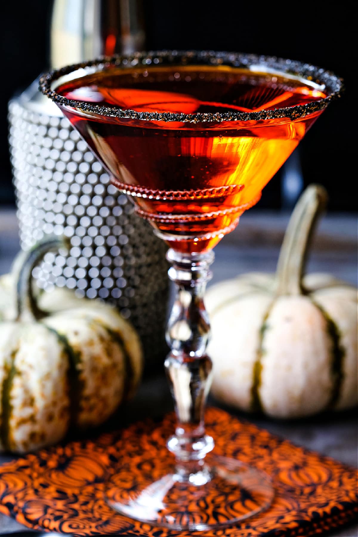 an orange martini in a sugar rimmed glass with pumpkins in the background