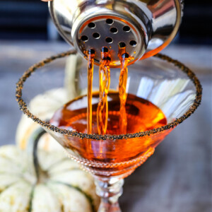 a cocktail shaker pouring out a pumpkin martini into a glass