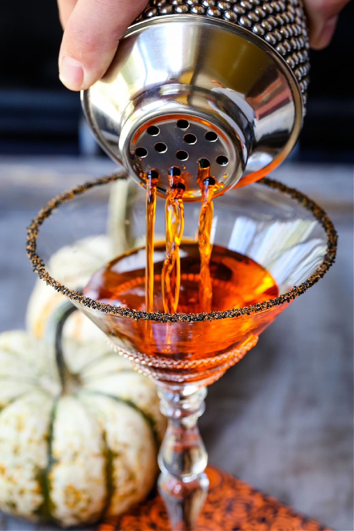 a cocktail shaker pouring out a pumpkin martini into a glass