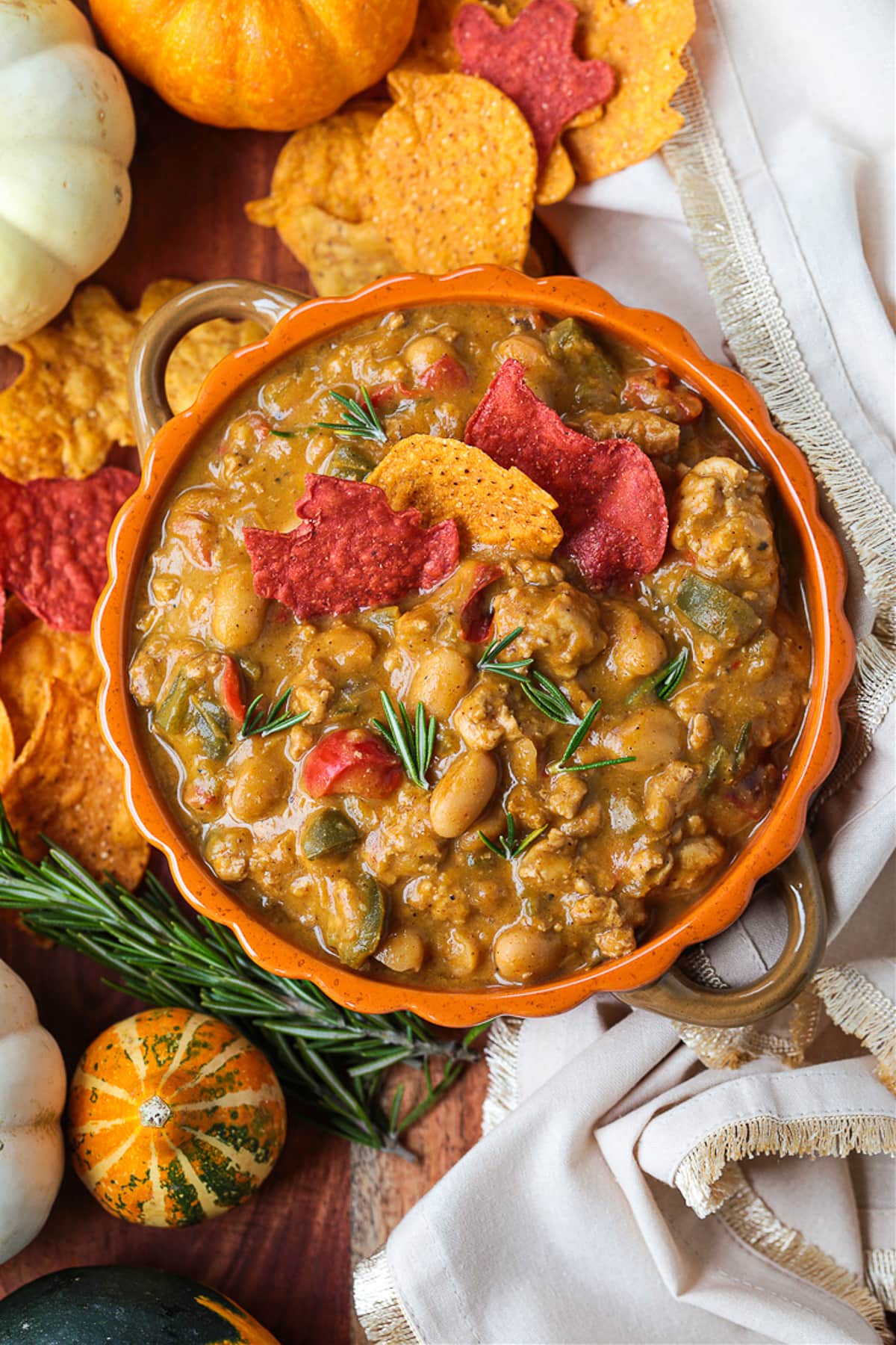 This cozy Pumpkin Chili recipe is giving all the fall vibes! A creamy, hearty turkey chili simmered with pumpkin puree, white wine and beans! Turkey chili in an orange bowl with pumpkin around