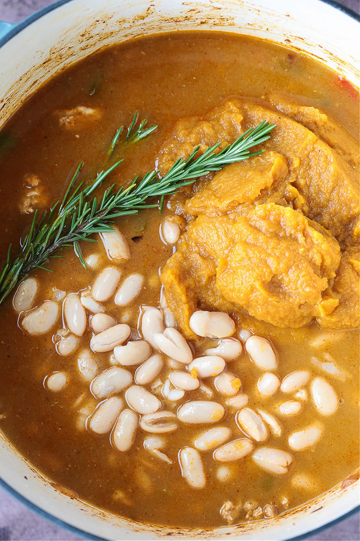 This cozy Pumpkin Chili recipe is giving all the fall vibes! A creamy, hearty turkey chili simmered with pumpkin puree, white wine and beans! white beans and pumpkin puree in a pot for making pumpkin chili
