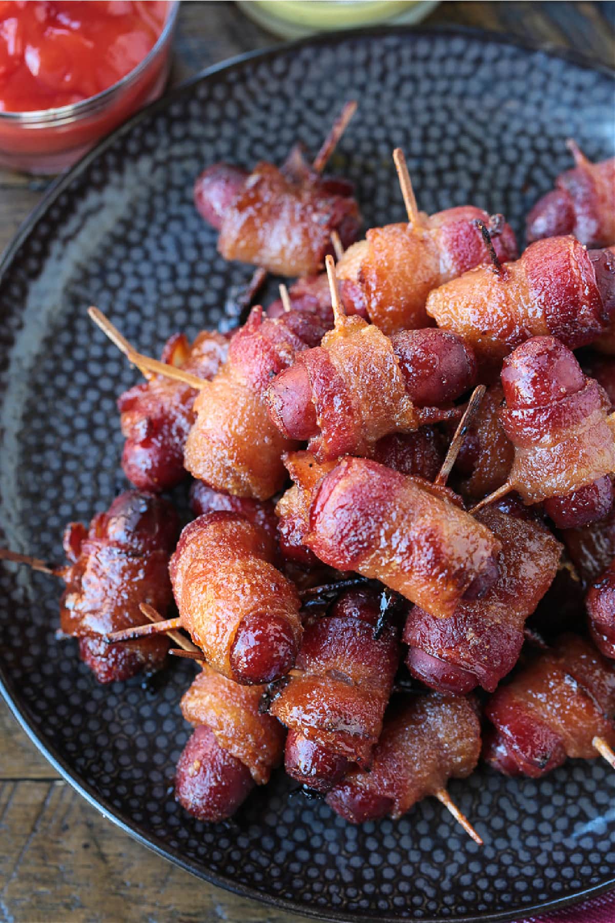 Bacon Wrapped Smokies are an addicting one-bite appetizer that everyone loves! Perfect for game days, parties and holidays! bacon wrapped hot dogs on black plate