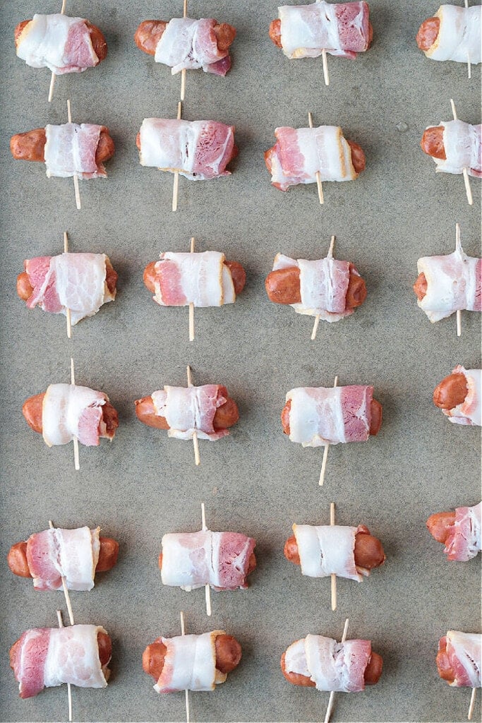 mini hot dogs wrapped in bacon on sheet pan