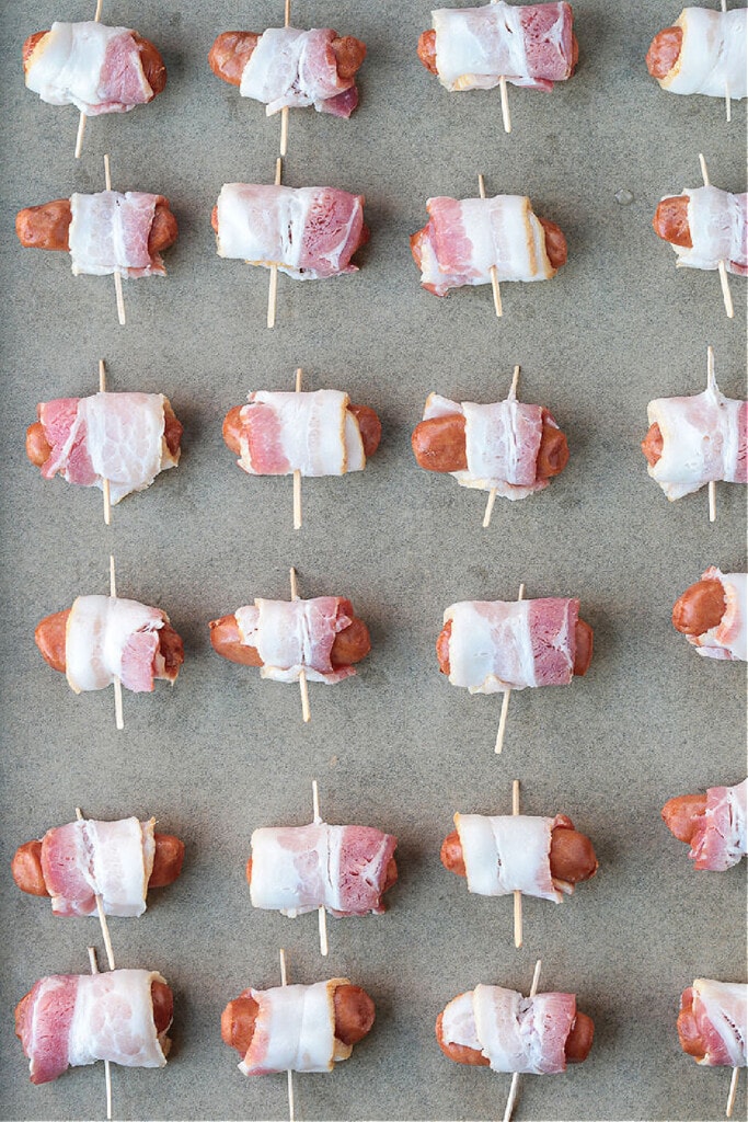 Bacon Wrapped Smokies are an addicting one-bite appetizer that everyone loves! Perfect for game days, parties and holidays! mini hot dogs wrapped in bacon on sheet pan
