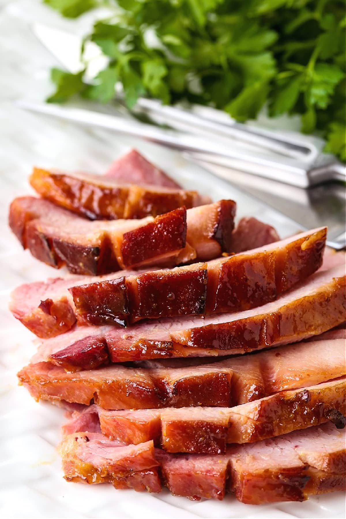 slices of ham on a white platter with fork and knife