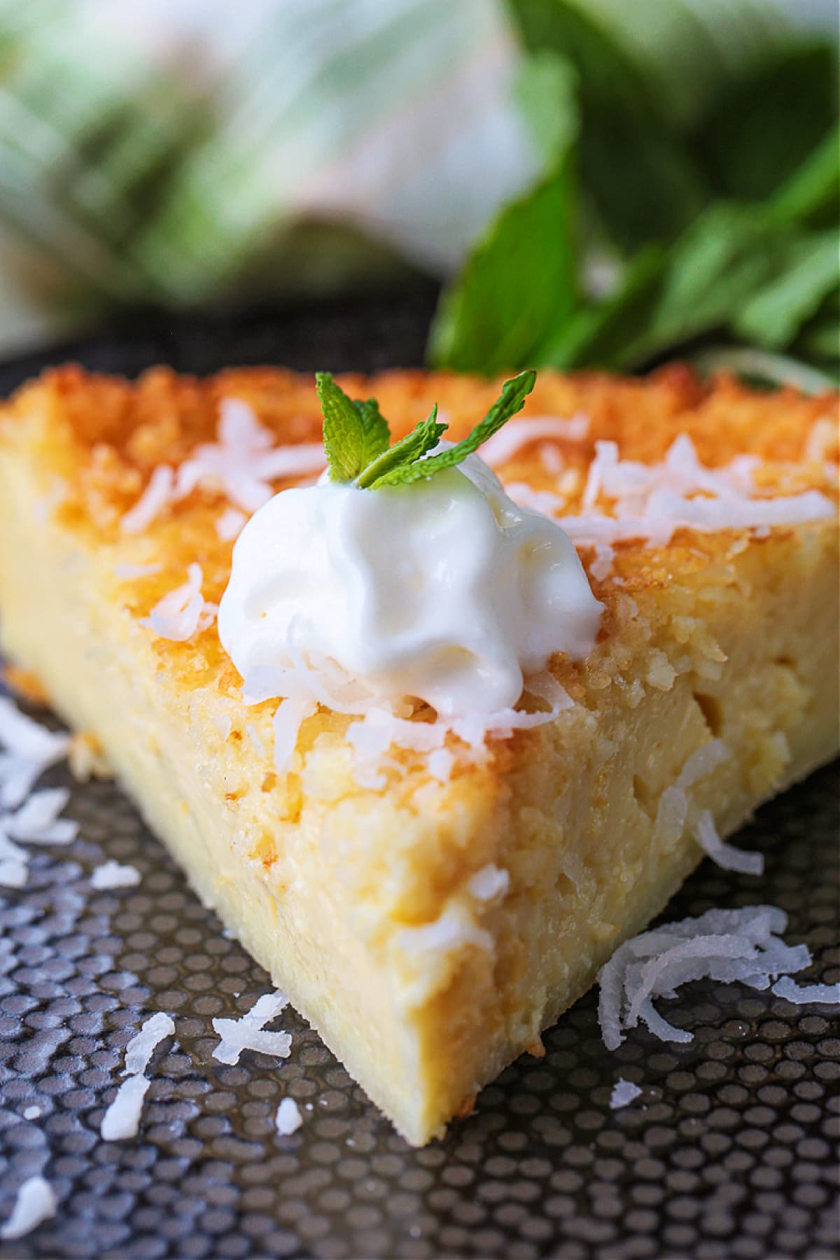 Impossible Coconut Pie is so easy to make it seems impossible! A creamy, sweet, custard pie that forms it's own crust as it bakes! slice of coconut pie with whipped cream and mint