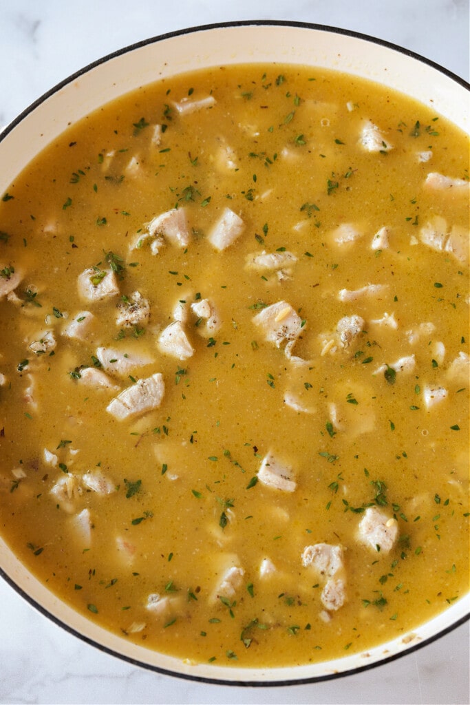 chicken broth in skillet with diced chicken and orzo