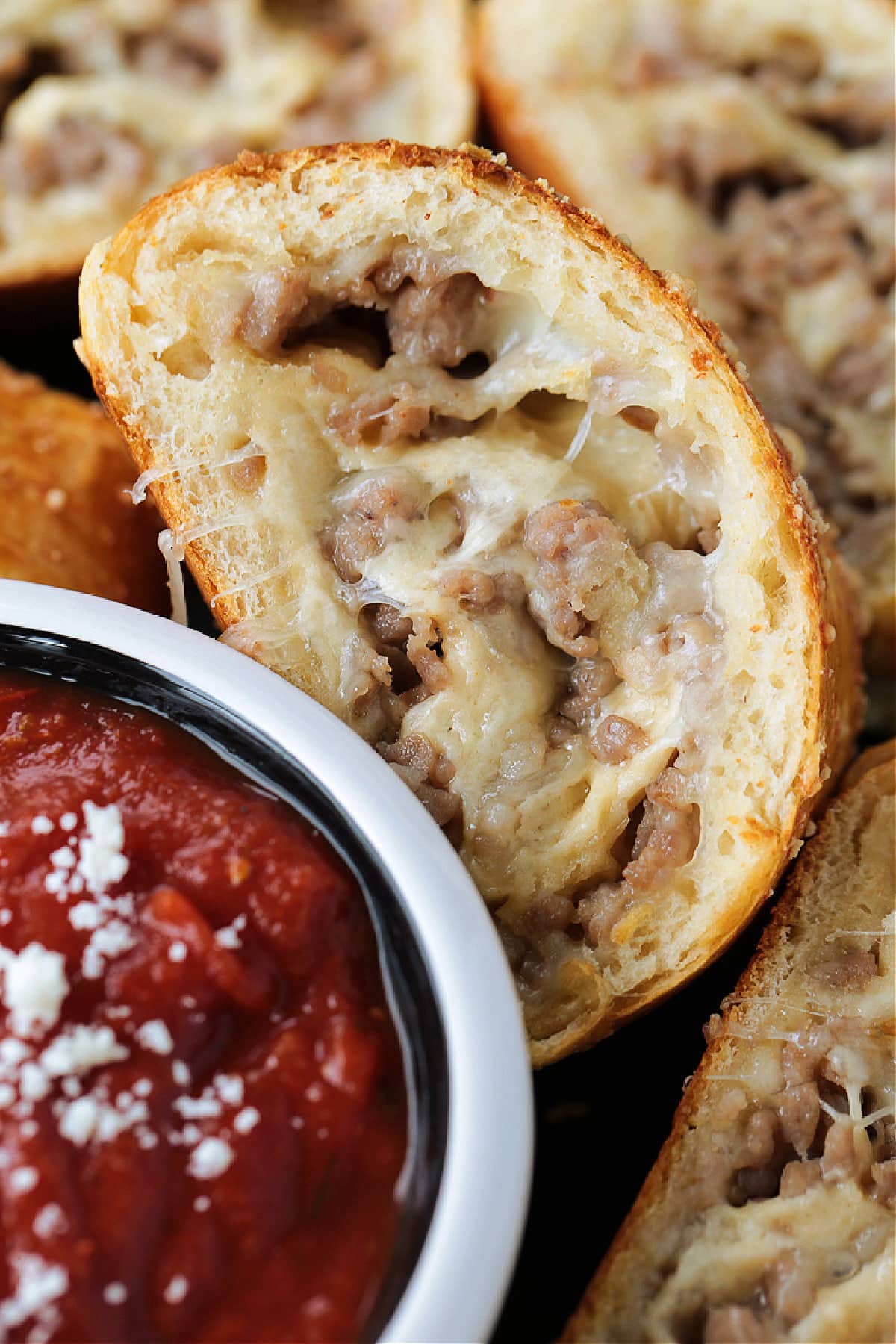 Our Sausage Bread recipe is packed full of sausage and cheese. Slice and serve for appetizers or for a fun dinner night instead of pizza. slices of sausage bread on platter with marinara sauce