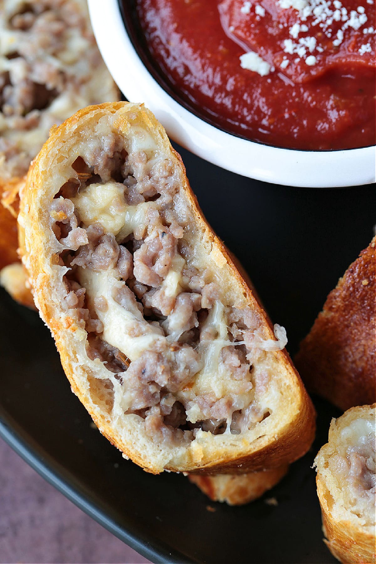 Our Sausage Bread recipe is packed full of sausage and cheese. Slice and serve for appetizers or for a fun dinner night instead of pizza. close up of a slice of sausage bread next to marinara sauce