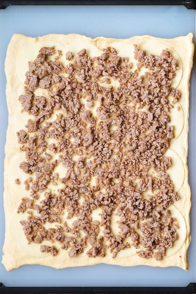 Our Sausage Bread recipe is packed full of sausage and cheese. Slice and serve for appetizers or for a fun dinner night instead of pizza. crumbled sausage on rolled out crescent roll dough