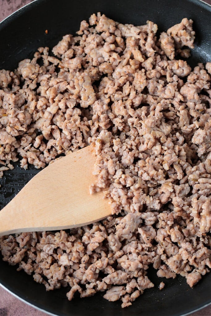 Our Sausage Bread recipe is packed full of sausage and cheese. Slice and serve for appetizers or for a fun dinner night instead of pizza. crumbles of sausage in a skillet with wooden spoon