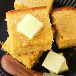 squares of cornbread on a black plate with butter knife