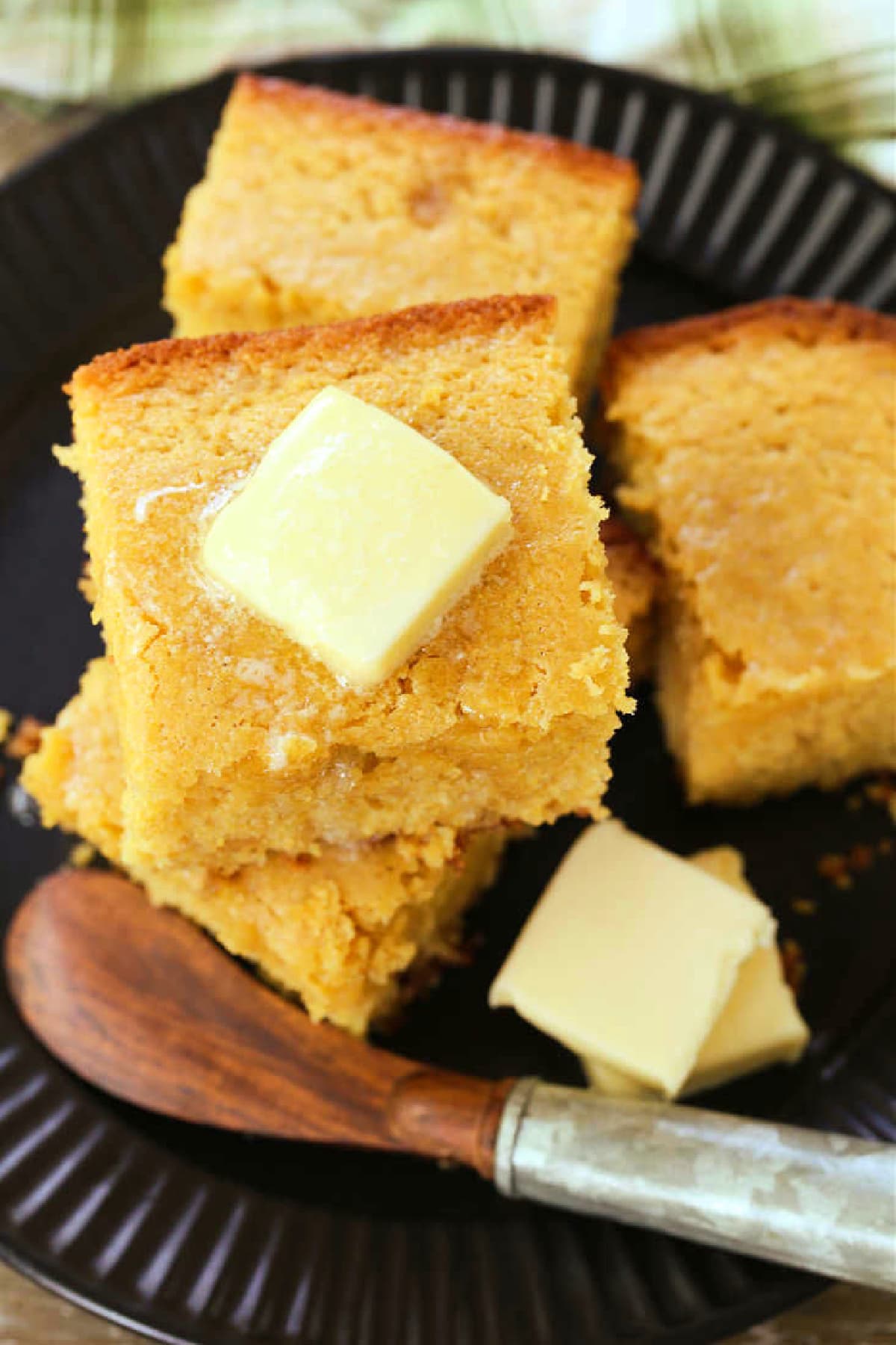 Sweet Cornbread is so moist and addicting. This sweet cornbread recipe is an easy side dish for chili, pulled pork or a holiday ham dinner! squares of cornbread on a black plate with butter knife