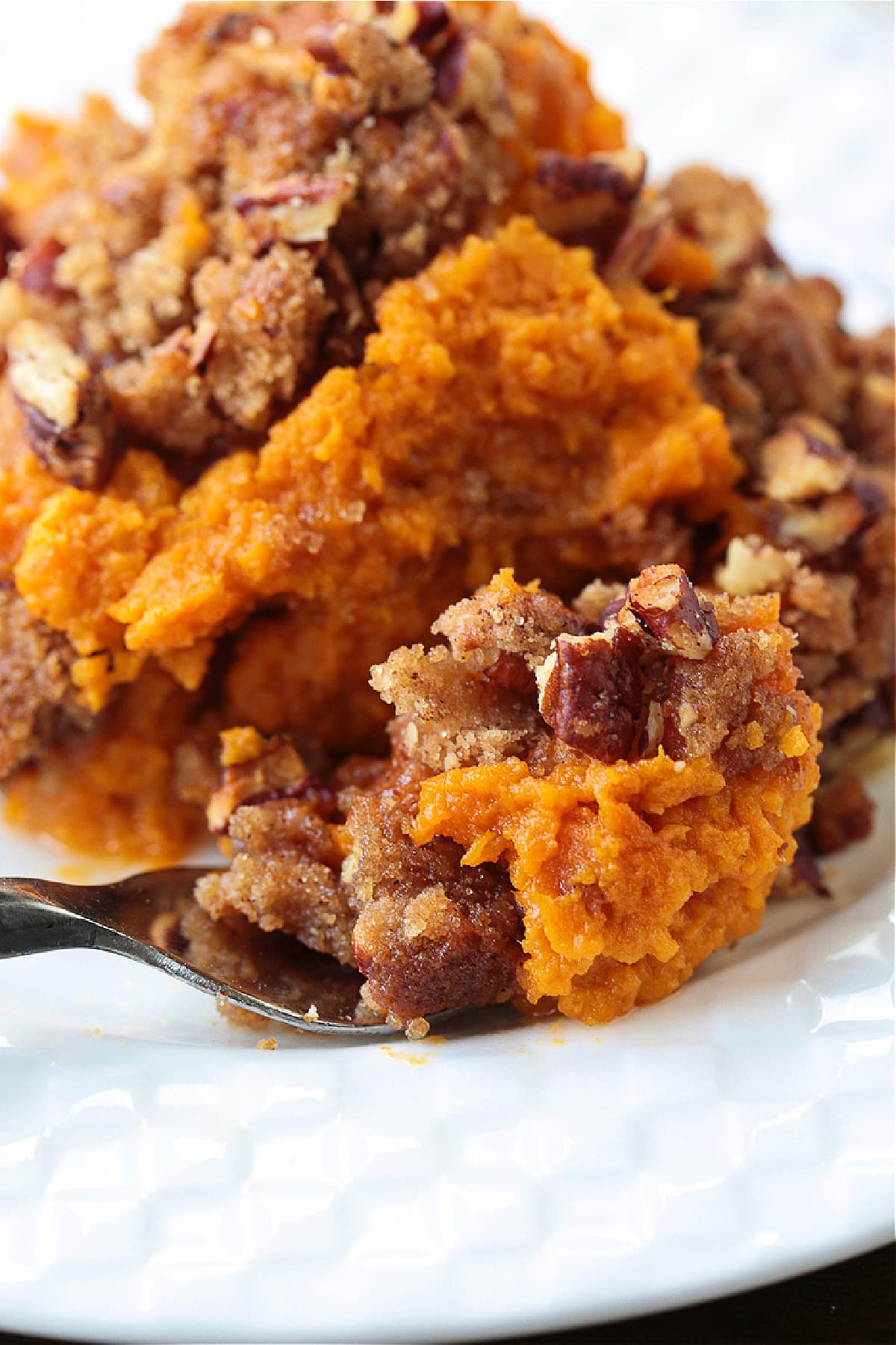 Our Sweet Potato Souffle is light and fluffy with a sweet, nutty streusel topping! A make ahead side dish for all of your holiday dinners! sweet potato souffle in white plate with fork