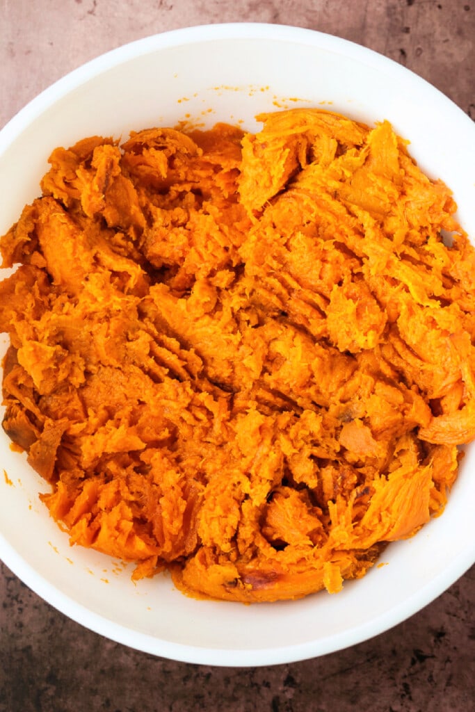 Our Sweet Potato Souffle is light and fluffy with a sweet, nutty streusel topping! A make ahead side dish for all of your holiday dinners! mashed sweet potatoes in white bowl