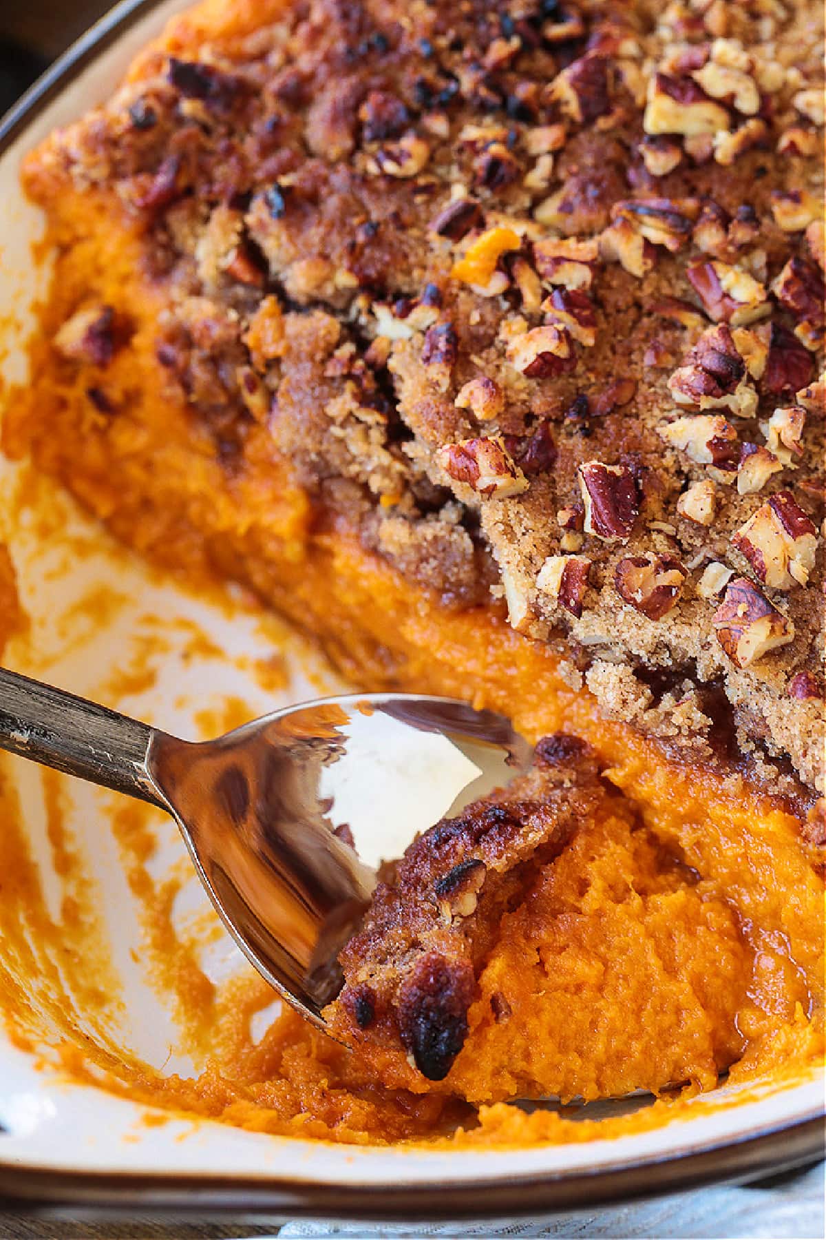 Our Sweet Potato Souffle is light and fluffy with a sweet, nutty streusel topping! A make ahead side dish for all of your holiday dinners! spoon in baking dish with sweet potato souffle