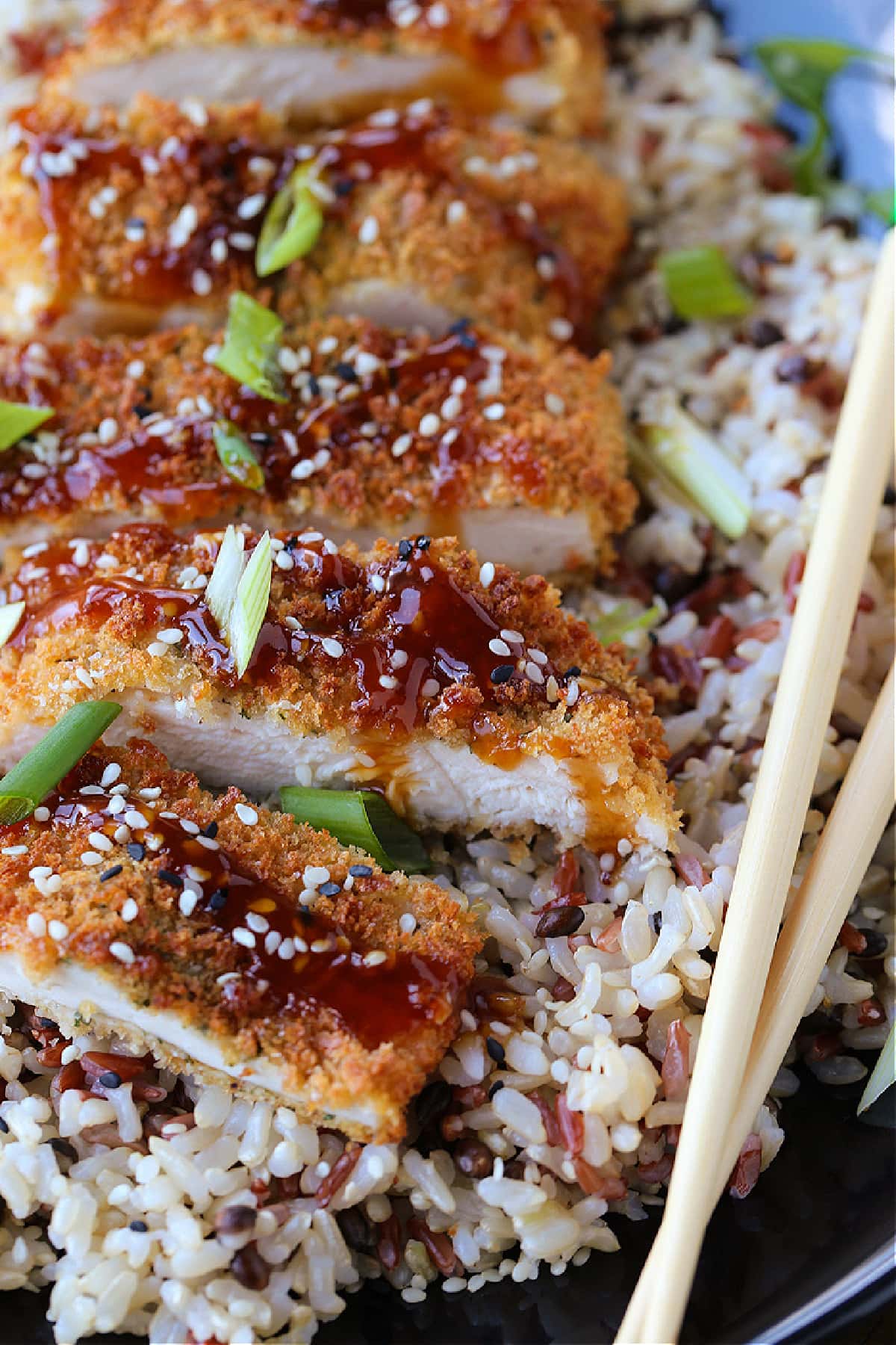 Air Fryer Chicken Katsu tastes as good as the fried version! Slice and drizzle with Asian BBQ sauce (Tonkatsu) and serve on a bed of rice. chicken katsu on a plate with rice and chop sticks