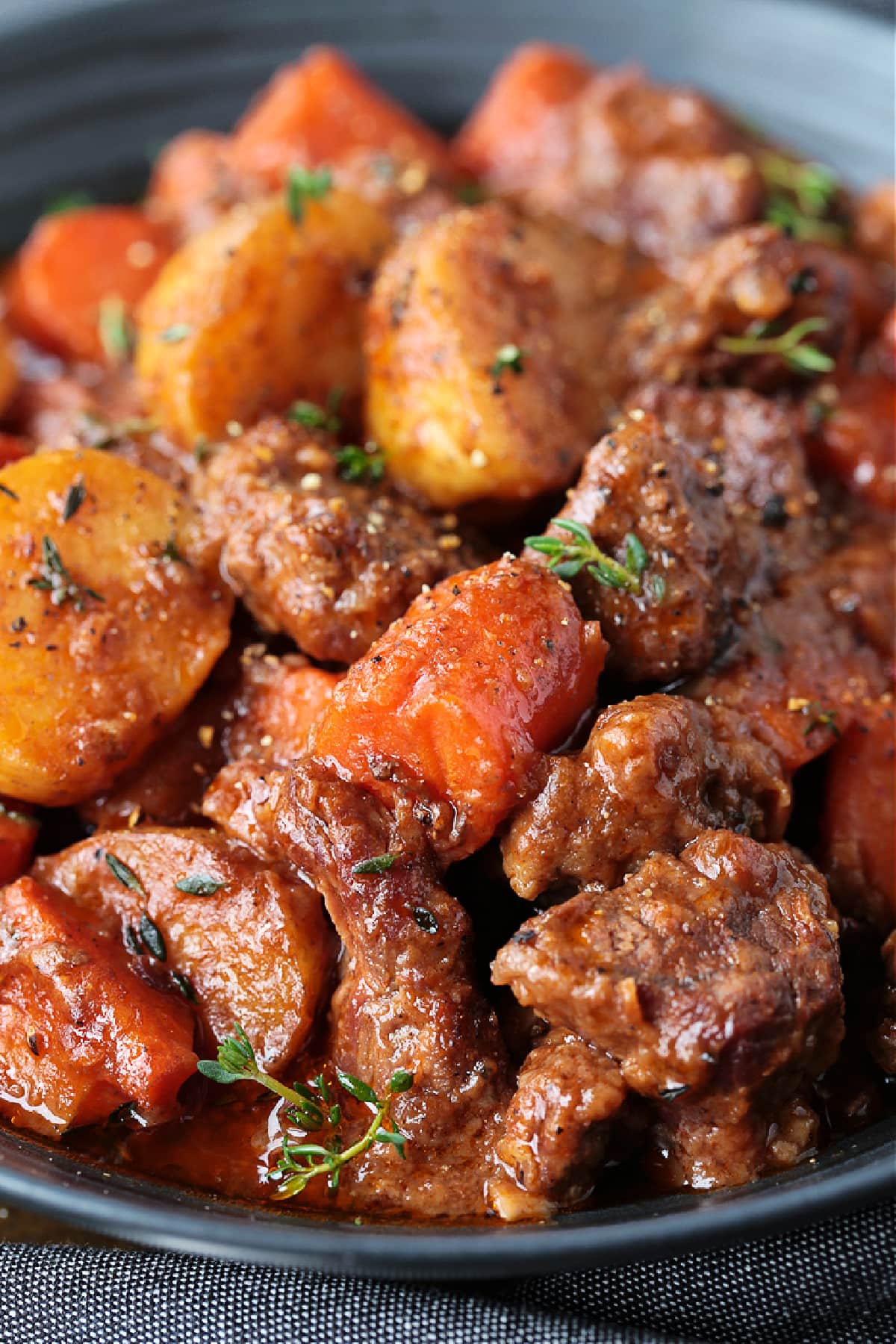 Our Easy Beef Stew is sure to become a family favorite! Tender pieces of beef and vegetables simmered in a red wine and beef gravy. close up of beef stew on a black plate