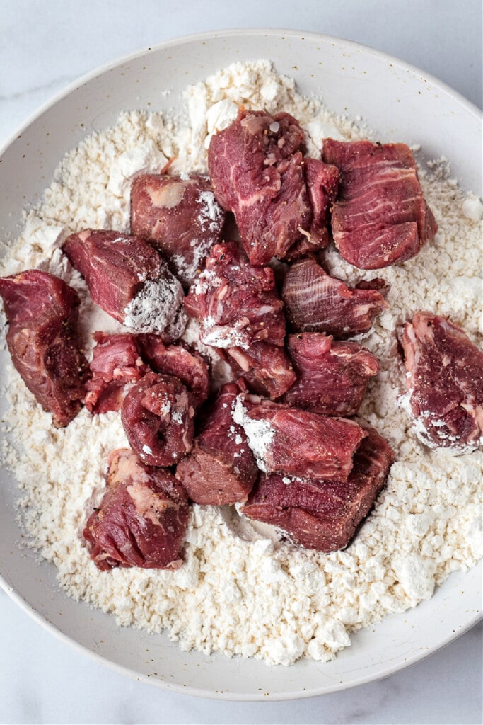Our Easy Beef Stew is sure to become a family favorite! Tender pieces of beef and vegetables simmered in a red wine and beef gravy. cubes of beef on a plate with flour