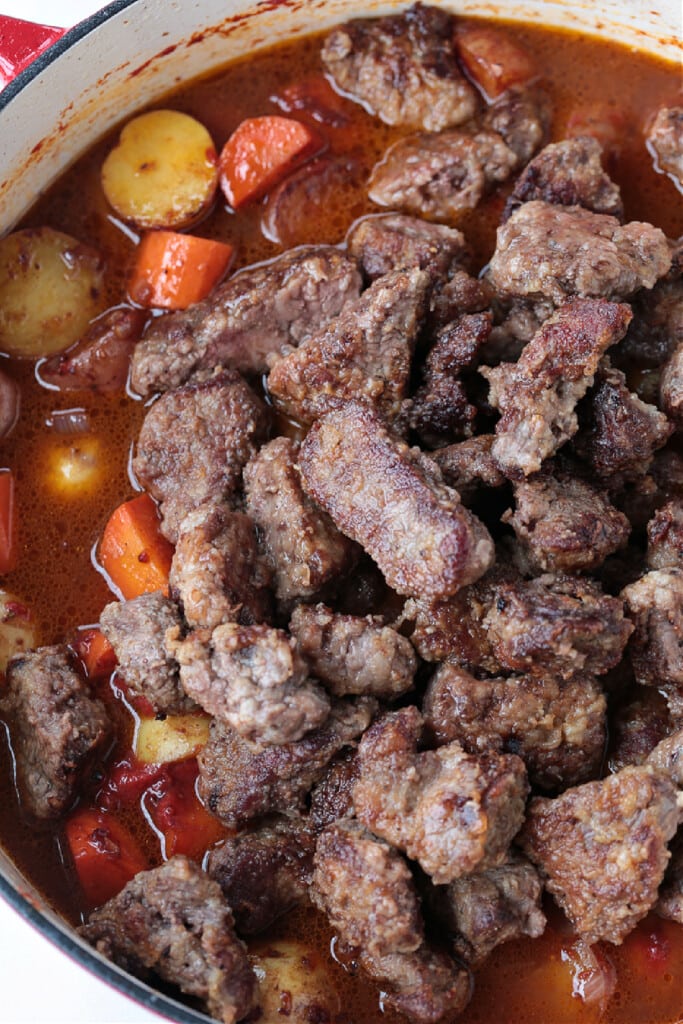 browned meat added to a pot of stew