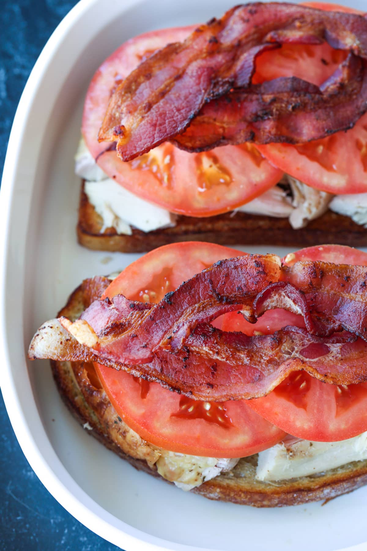 A Kentucky Hot Brown Sandwich is a delicious way to use leftover turkey. Baked with slices of tomato and bacon smothered in a cheesy sauce! slices of cooked bacon on top of tomatoes and turkey in baking dish