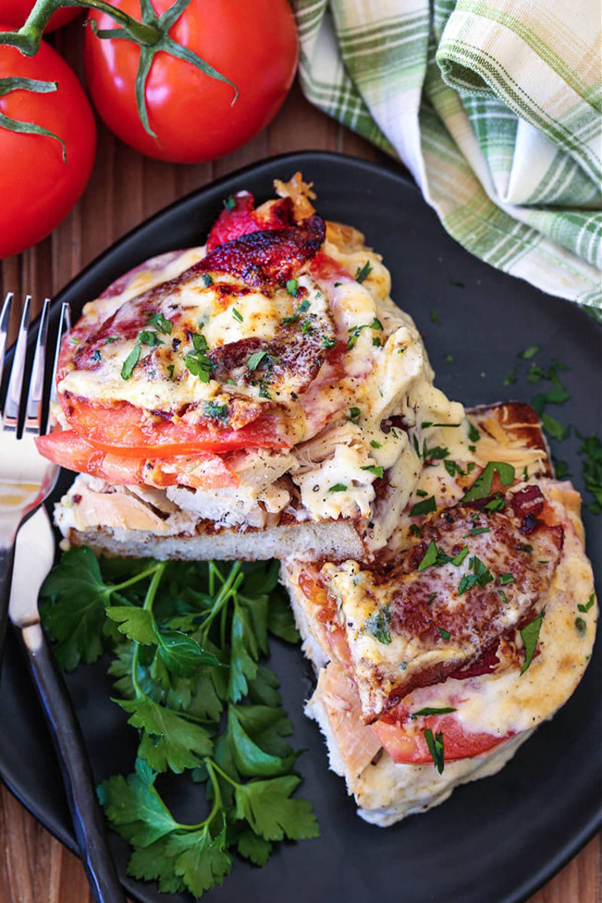 A Kentucky Hot Brown Sandwich is a delicious way to use leftover turkey. Baked with slices of tomato and bacon smothered in a cheesy sauce! open faced turkey sandwich with bacon and tomato on black plate