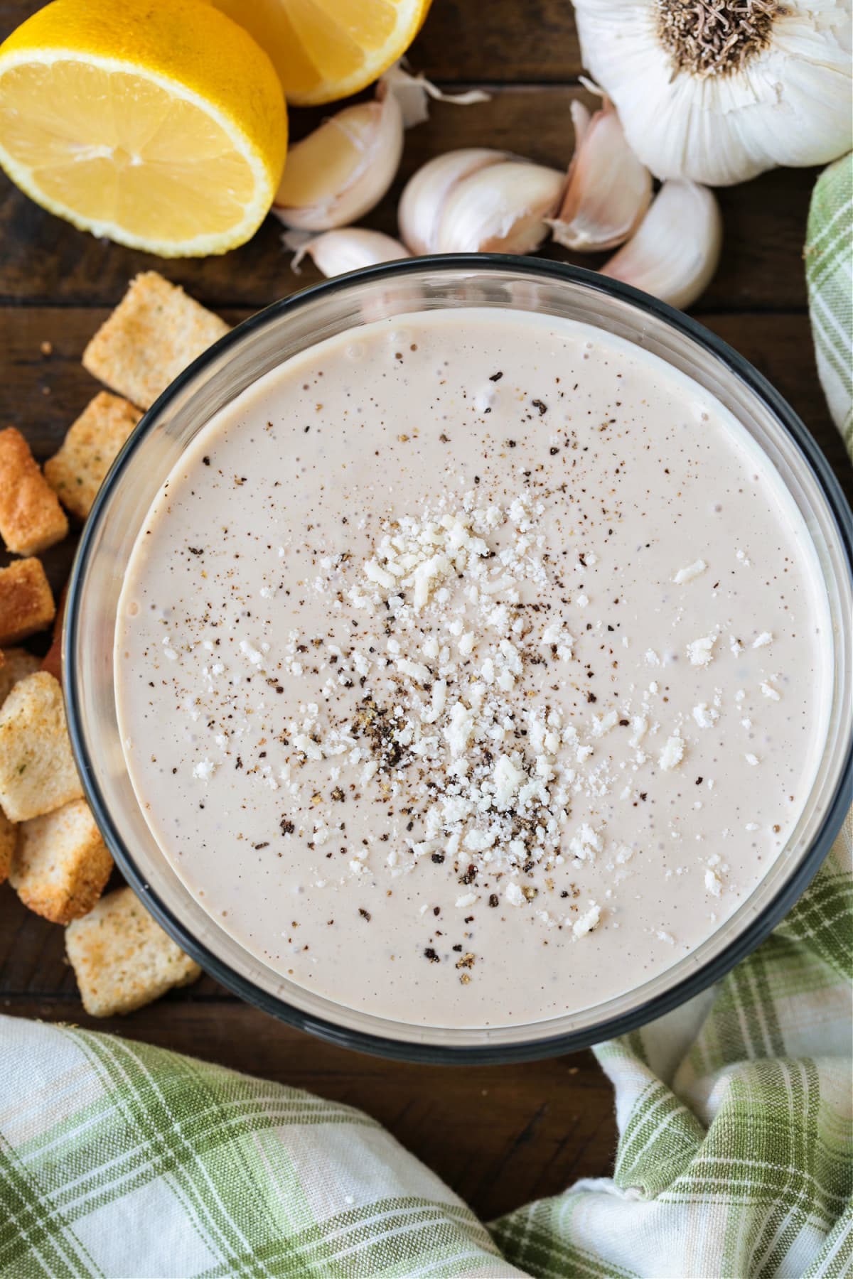 creamy caesar dressing in bowl with croutons, garlic and lemon on side