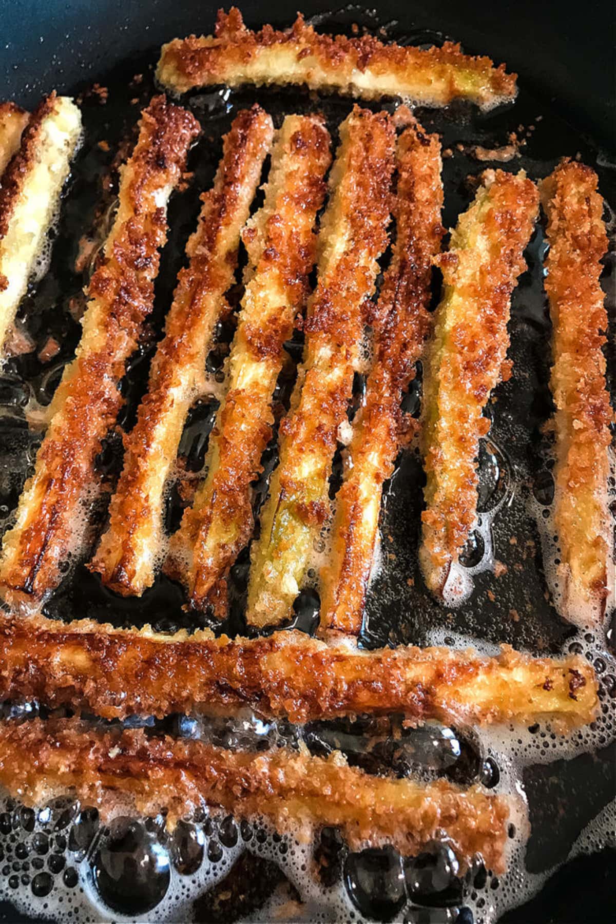 Crispy Eggplant Fries are so addicting! Breaded, lightly fried eggplant strips topped with parmesan cheese and dipped into marinara sauce. breaded eggplant fries frying in a skillet