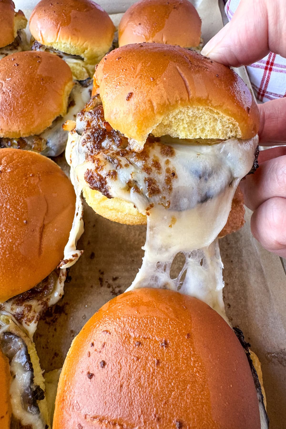 Our French Dip Sliders have a secret sauce that sets them apart from the rest. Beefy, cheesy comfort food perfect for parties and game days! A cheese and roast beef slider being pulled from a sheet pan