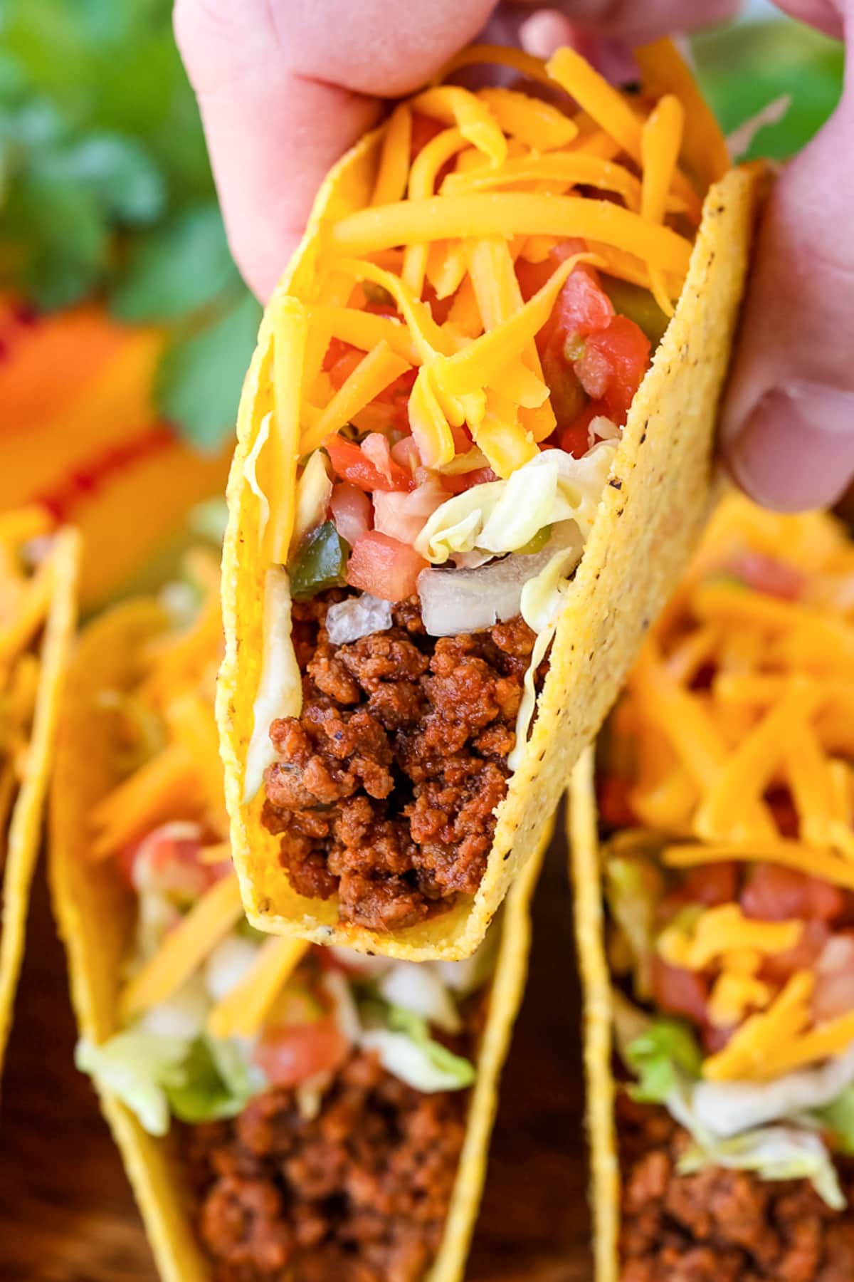 Make taco night even better with our homemade Ground Beef Taco Meat! 15 minutes is all you need to have the most delicious, homemade tacos! taco being lifted with tacos in the background