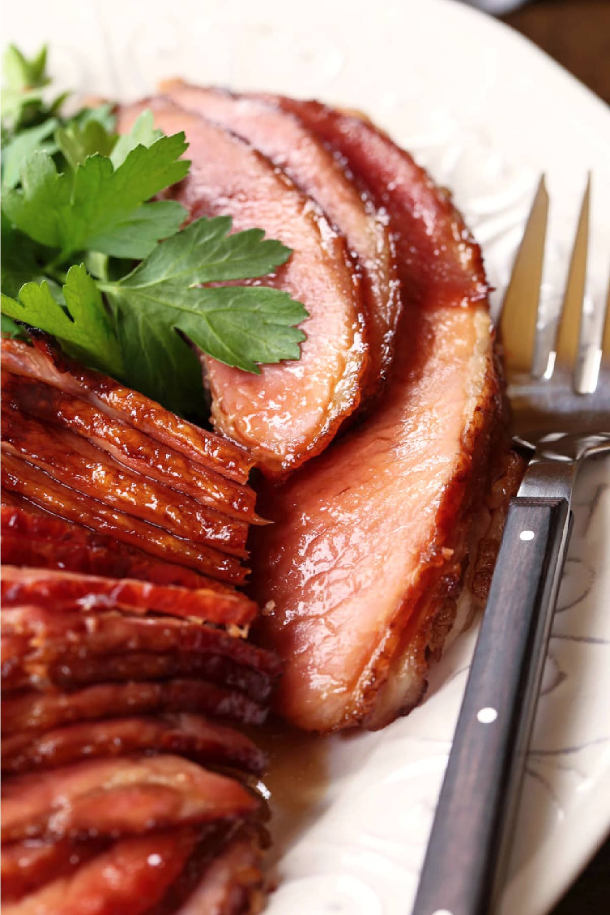 sliced spiral ham on a white platter with serving fork and parsley