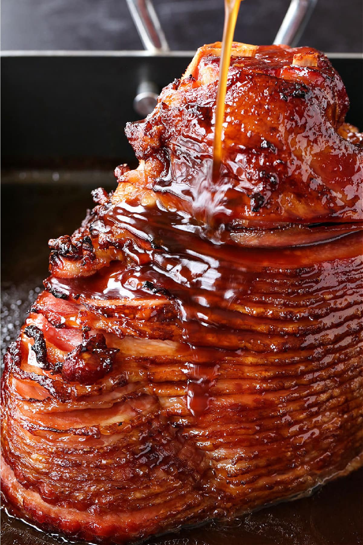 spiral sliced ham in roasting pan with glaze being poured over