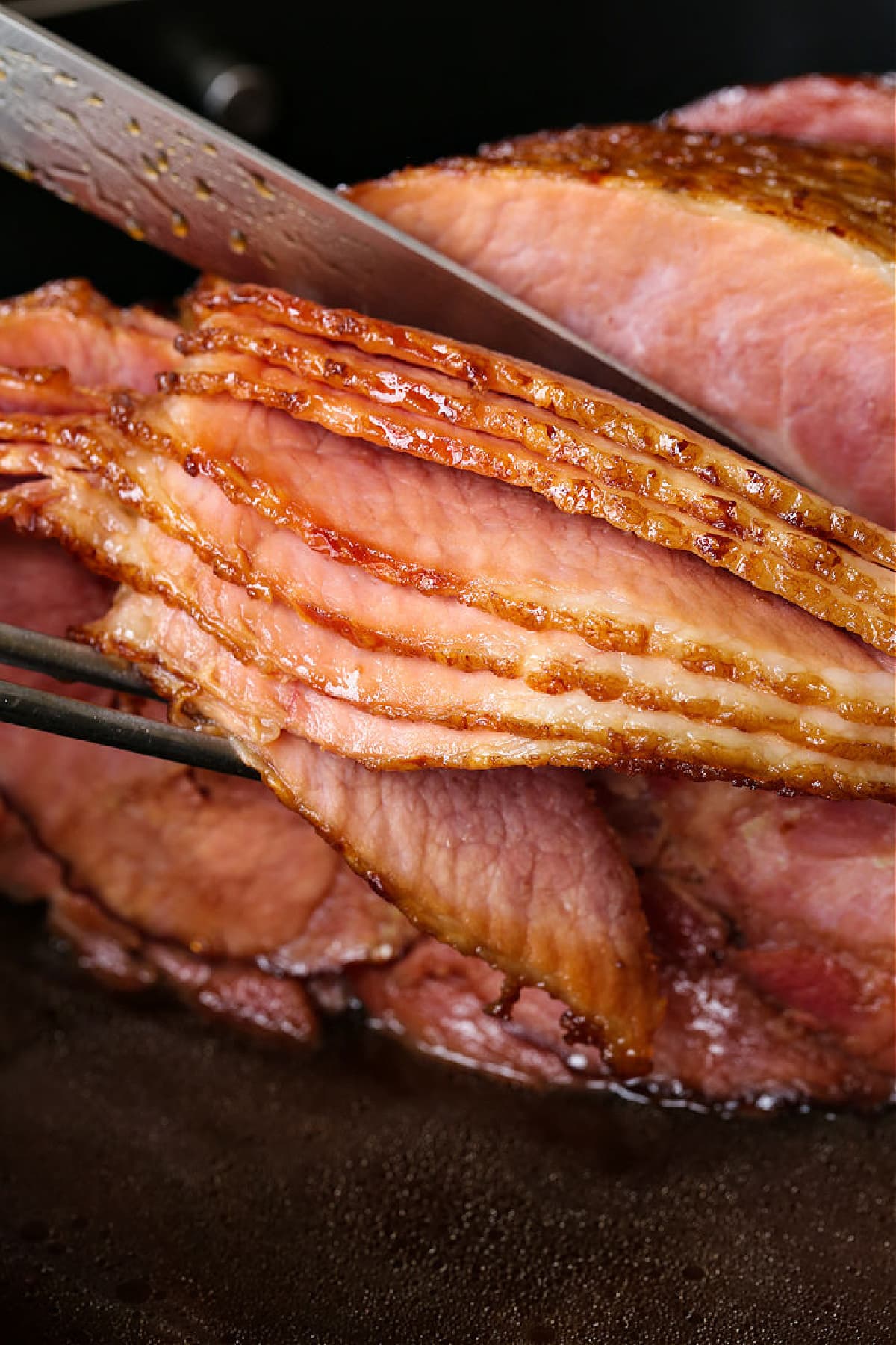 Bourbon Glazed Ham is a holiday favorite! A sweet caramelized glaze paired with the smoky taste of bourbon baked into layers of tender ham. sliced ham being served with a fork and knife