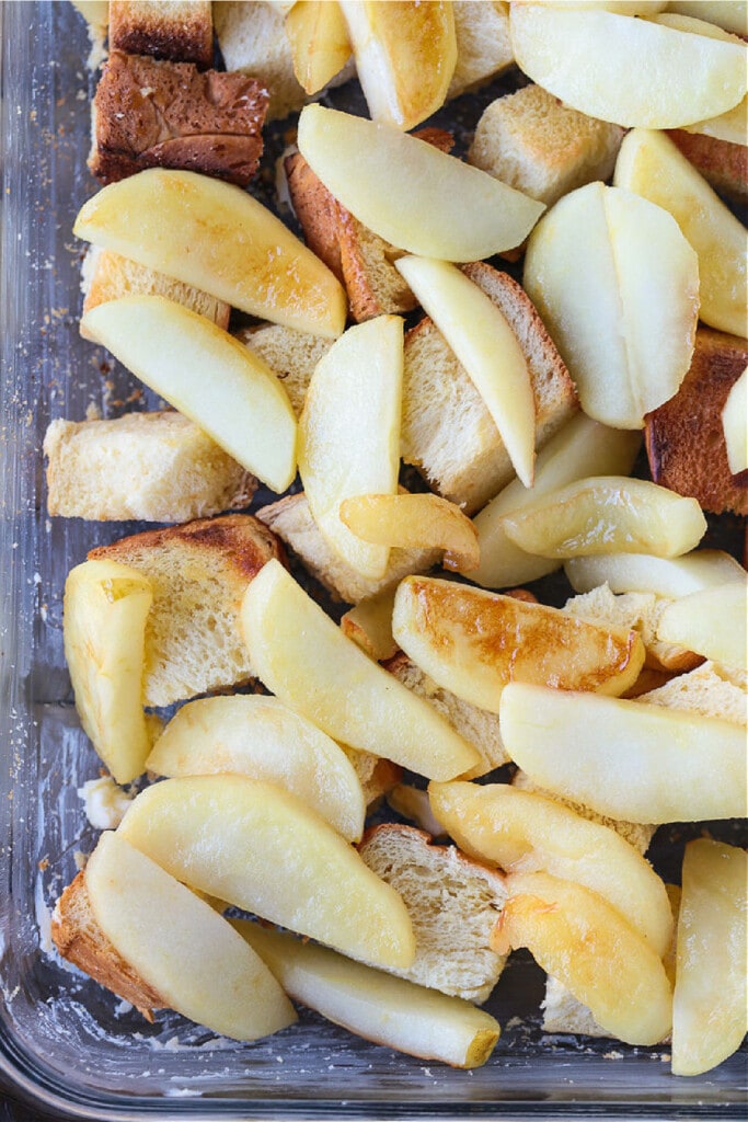 Cozy Apple Bread Pudding is one of our favorite fall desserts! Sweet, brioche bread soaked in a rich custard layered with buttery apples! sliced apples and brioche bread cubes in dish for bread pudding