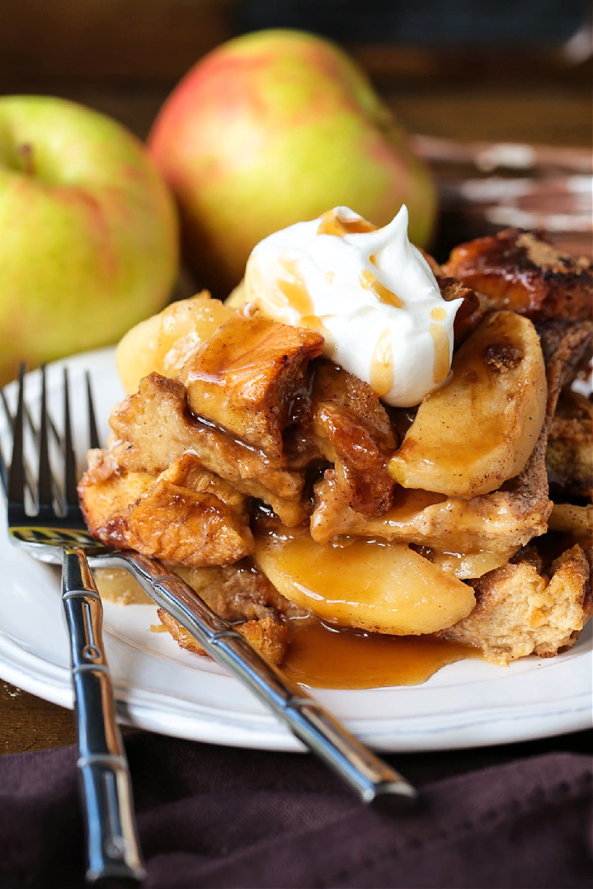 Cozy Apple Bread Pudding is one of our favorite fall desserts! Sweet, brioche bread soaked in a rich custard layered with buttery apples! slice of apple bread pudding on plate with whipped cream