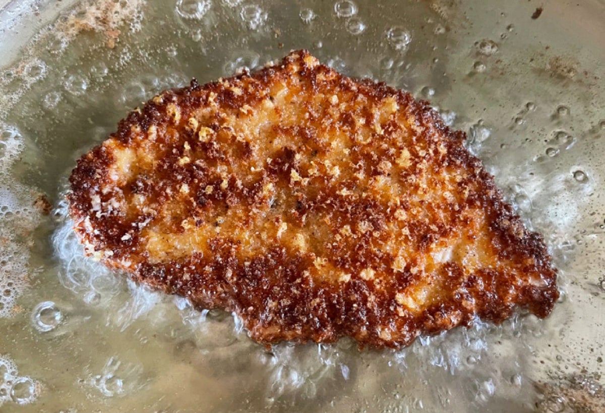 Sesame Chicken Milanese is a delicious twist on the classic chicken recipe! Thin, crispy chicken cutlets topped with crisp greens and an Asian vinaigrette! brown and crispy chicken cutlet frying in oil