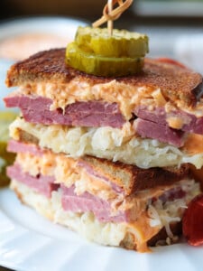 reuben sandwich stacked on a plate with pickles