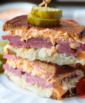 reuben sandwich stacked on a plate with pickles