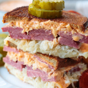 reuben sandwich stacked on a plate with pickles