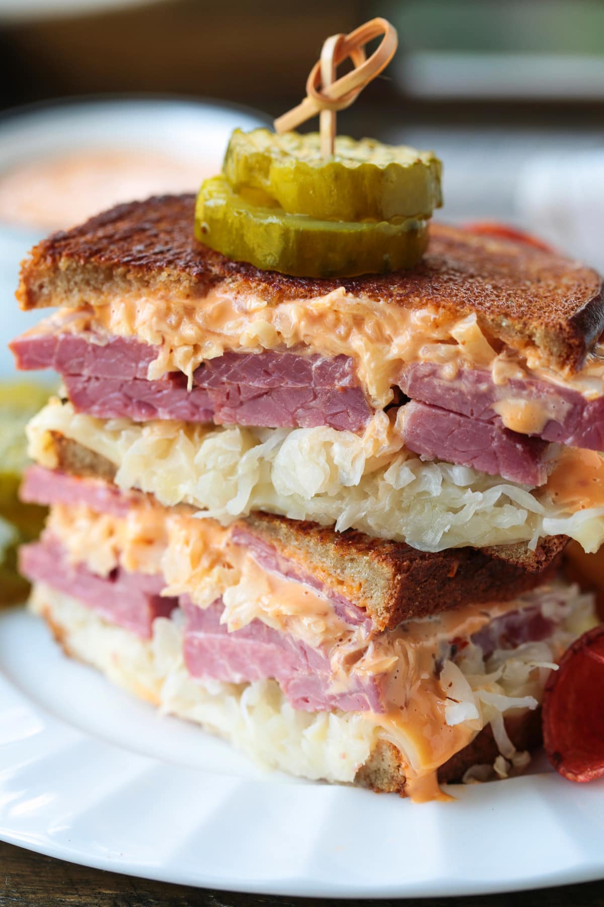 reuben sandwich stacked on a plate with pickles