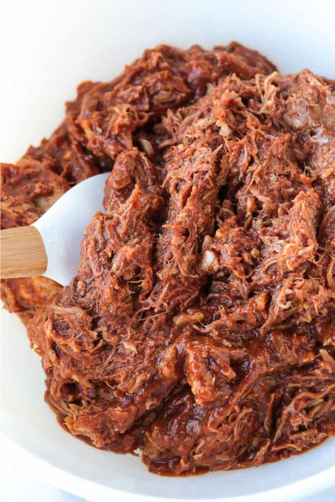 barbecue pulled pork in a white bowl with spatula