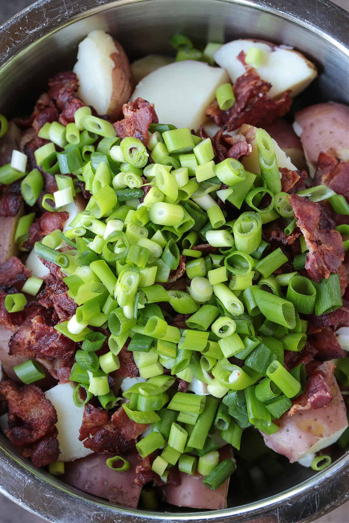 Ranch Potato Salad is a delicious, make ahead side dish! A hearty and tangy potato salad with creamy red potatoes and thick, crisp bacon. chopped scallions and bacon in a bowl with potatoes