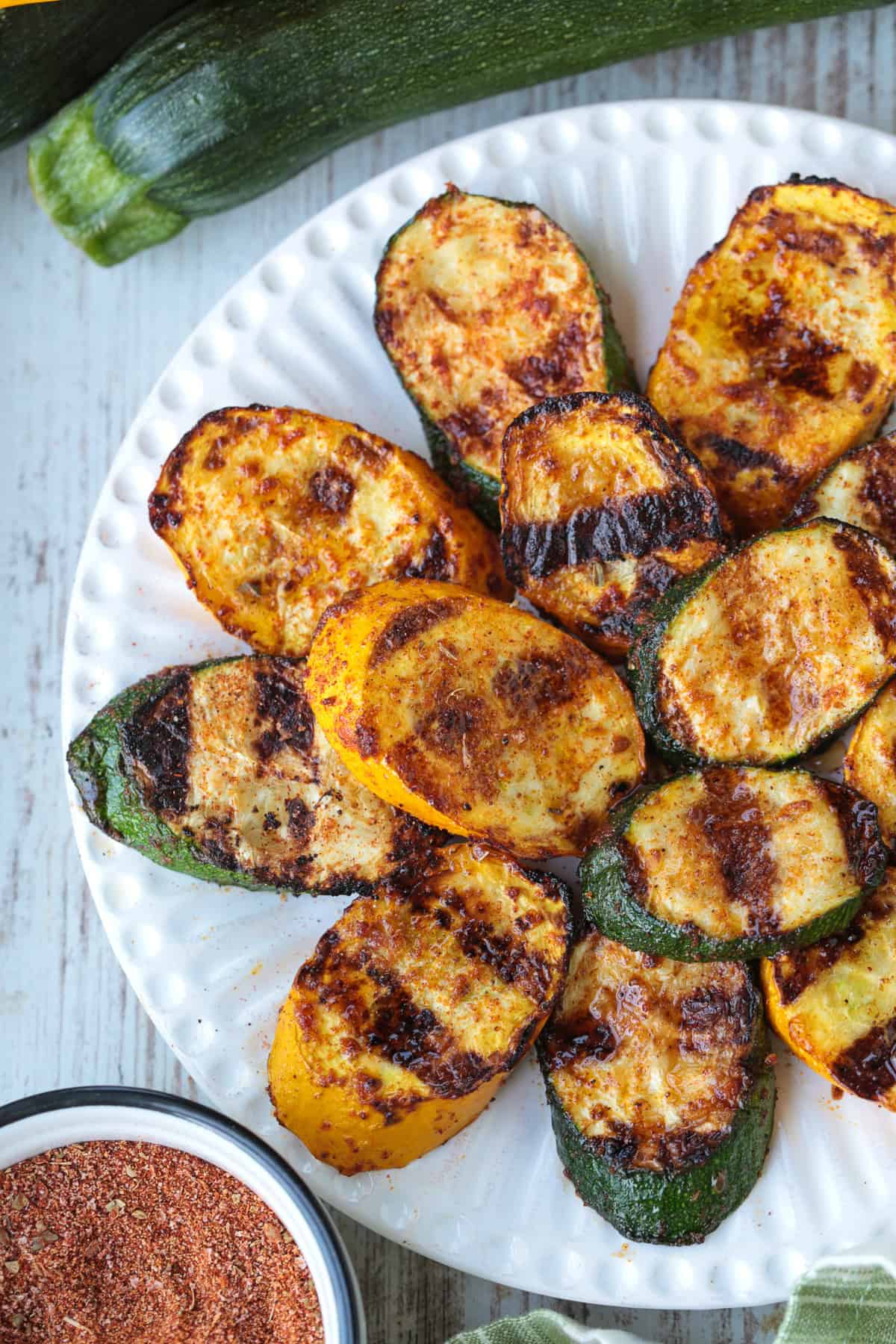 Grilled Zucchini and Squash is an easy side dish for any meal! Seasoned with our all purpose spice blend and grilled to perfection! grilled slices of zucchini and yellow squash on white plate